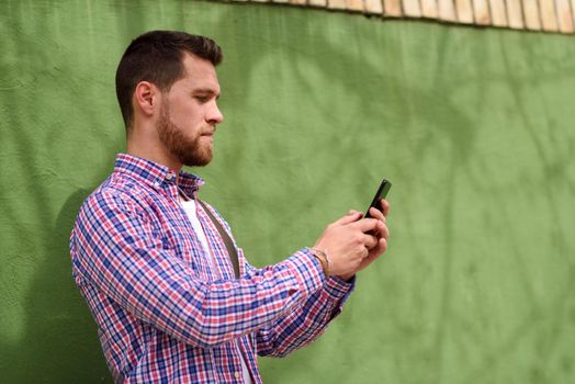 Young man looking at his smart phone in urban background. Guy wearing casual clothes. Lifestyle concept.