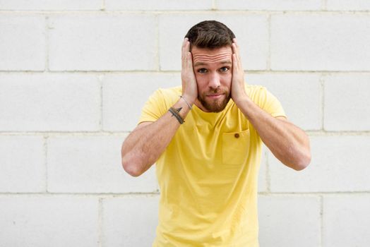 Funny young man on brick wall with funny expression covering his ears. Guy with winner gesture.