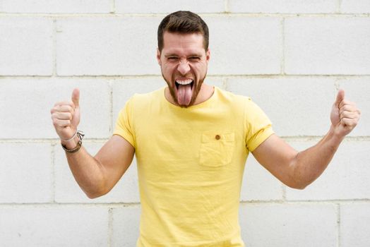 Funny young man on brick wall with funny expression. Guy sticking out tongue.