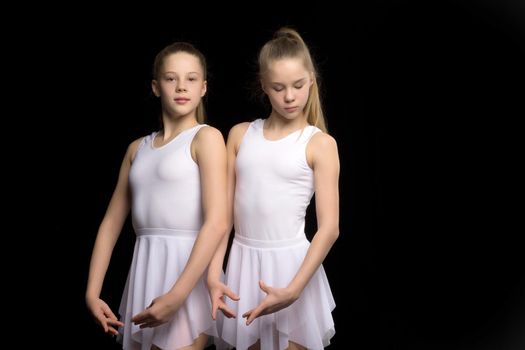 Two charming gymnasts in beautiful sports swimsuits posing in the studio. The concept of children's sports, fitness. Isolated on a black background.