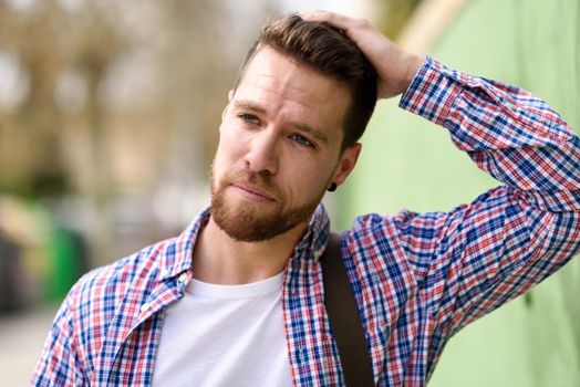 Thoughtful young man standing in urban background. Guy looking away wearing casual clothes. Lifestyle concept.