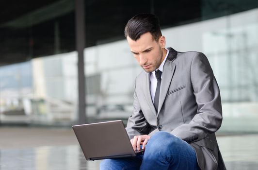 Portrait of attractive young businessman typing in a laptop computer in office building