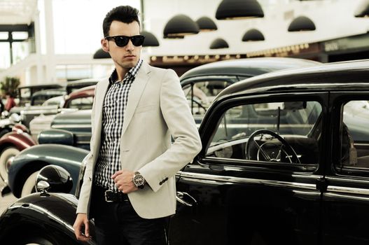 Portrait of a young handsome man, model of fashion, wearing jacket and shirt with old cars