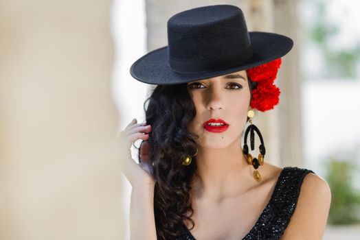 Portrait of beautiful woman, model of fashion, wearing spanish hat and red carnations in her hair