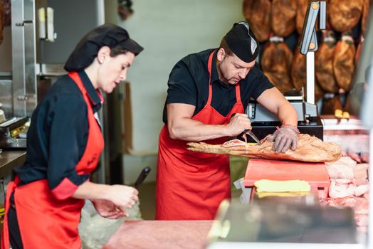 Male and female butchers boning a ham in a modern butcher shop