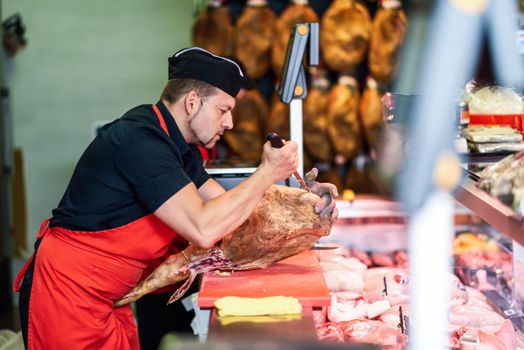 Male butcher boning a ham in a modern butcher shop
