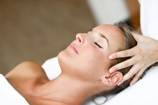 Young blond woman receiving a head massage in a spa center with eyes closed. Female patient is receiving treatment by professional therapist.