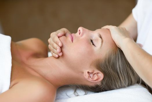 Young blond woman receiving a head massage in a spa center with eyes closed. Female patient is receiving treatment by professional therapist.