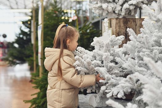 A girl and a white christmas artificial trees for sale on a shop