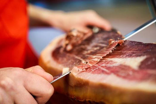 Close-up of professional cutter carving slices from a whole bone-in serrano ham