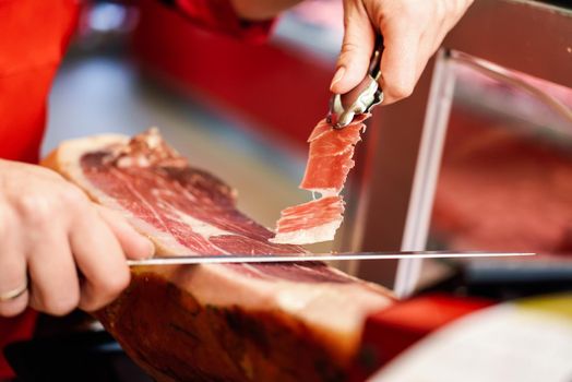 Close-up of professional cutter carving slices from a whole bone-in serrano ham