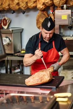 Male butcher boning a ham in a modern butcher shop with metal safety mesh glove