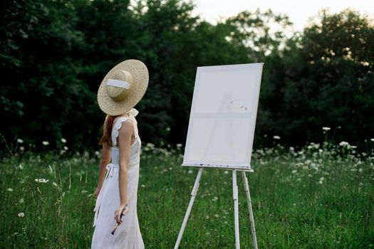 A woman in a white dress in a field with flowers paints a picture. High quality photo