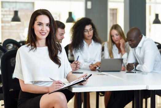 Multi-ethnic group of five businesspeople meeting in a modern office. Caucasian businesswoman leader, wearing white shirt and black skirt, looking at camera.