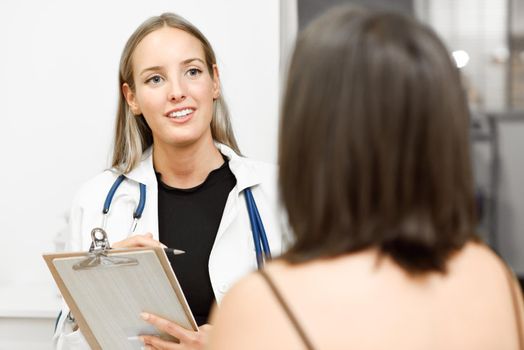 Female doctor explaining diagnosis to her patient. Brunette woman having consultation with smiling blonde girl in medical office.