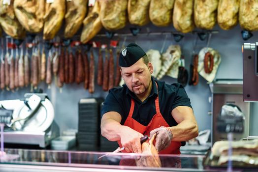 Male butcher boning a ham in a modern butcher shop with metal safety mesh glove