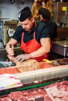 Male butcher boning a ham in a modern butcher shop with metal safety mesh glove