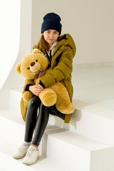 The concept of fashionable clothes for children. Beautiful little girl in a stylish coat with a teddy bear. Layout for the magazine. Isolated on a white background.