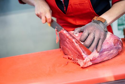 Female butcher cutting fresh meat in a butcher shop with metal safety mesh glove