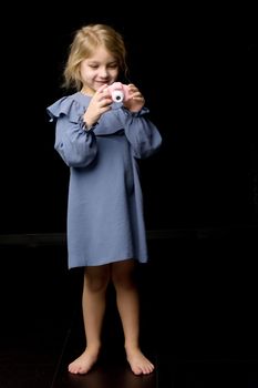 Beautiful Smiling Girl Taking Photo with Toy Camera, Adorable Barefoot Kid in Blue Dress Posing in Studio, Full Length Portrait of Cute Stylish Blonde Girl Isolated on Black Background