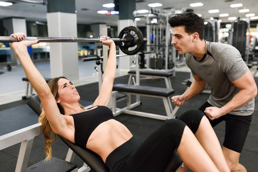 Personal trainer motivating a young woman lift weights while working out in a gym