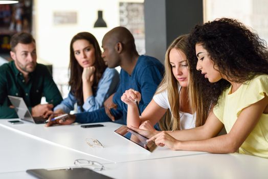 Five young people studying with tablet and laptop computer on white desk. Beautiful women and men working together wearing casual clothes. Multi-ethnic group.