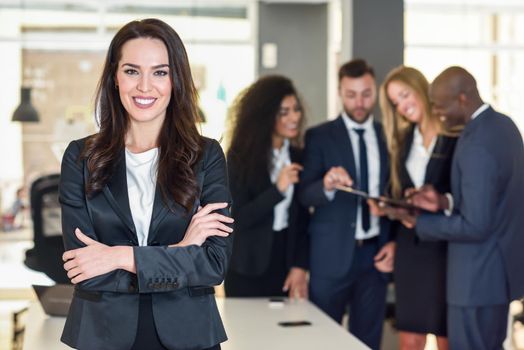 Businesswoman leader looking at camera in modern office with multi-ethnic businesspeople working at the background. Teamwork concept. Caucasian woman.