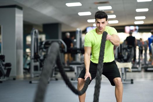 Man with battle ropes exercise in the fitness gym. Young male wearing sportswear.