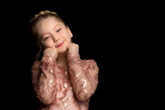 A charming little girl folded her hands around her face. The concept of beauty and fashion, children's emotions. Isolated on a black background.