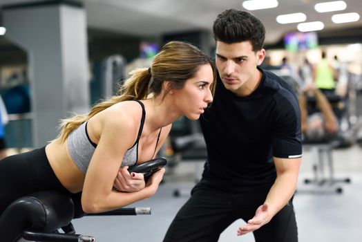 Personal trainer helping young woman lift weights while working out in a gym