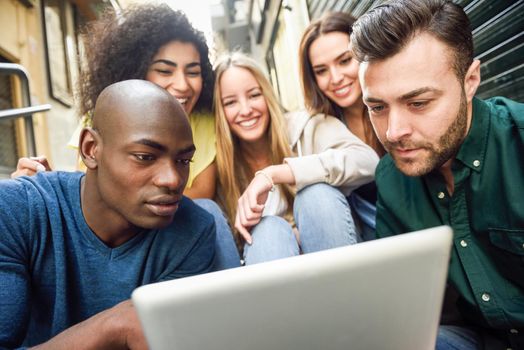 Multi-ethnic group of young people looking at a tablet computer outdoors in urban background. Group of men and woman sitting together on steps.