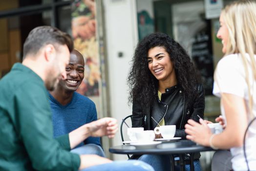 Multiracial group of four friends having a coffee together. Two women and and two men at cafe, talking, laughing and enjoying their time.