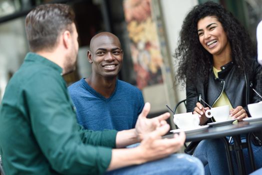 Multiracial group of three friends having a coffee together. A woman and two men at cafe, talking, laughing and enjoying their time. Lifestyle and friendship concepts with real people models