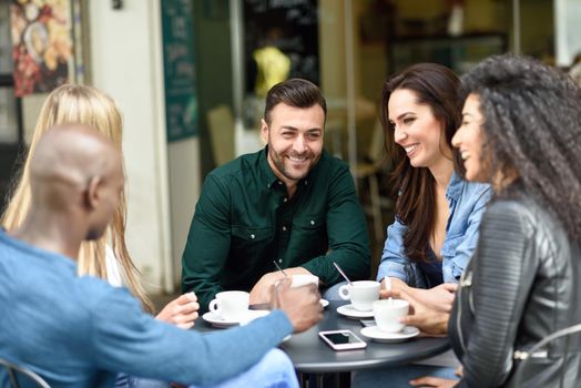 Multiracial group of five friends having a coffee together. Three women and two men at cafe, talking, laughing and enjoying their time. Lifestyle and friendship concepts with real people models