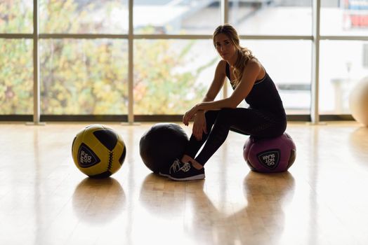 Woman sitting with fitballs in the gym. Young female wearing sportswear clothes.