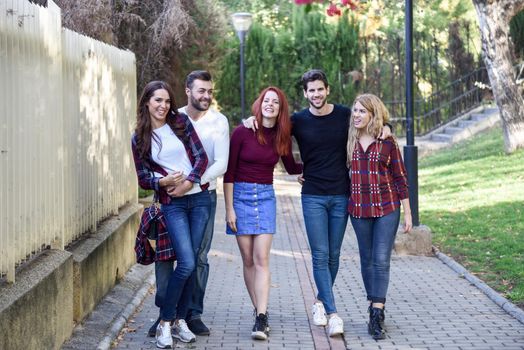 Group of young people together outdoors in urban background. Women and men sitting on stairs in the street wearing casual clothes.