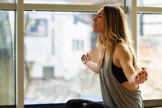 Young beautiful woman meditating in the lotus position in gym. Girl wearing sportswear clothes.