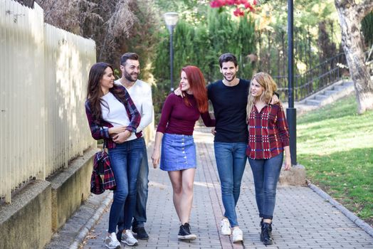 Group of young people together outdoors in urban background. Women and men sitting on stairs in the street wearing casual clothes.