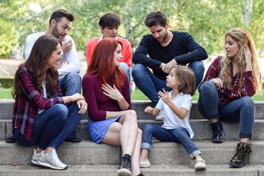 Young people together withe a little girl talking outdoors in urban background. Women and men sitting on stairs in the street wearing casual clothes.