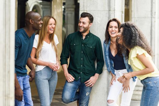 Multi-ethnic group of young people having fun together outdoors in urban background. group of beautiful women and men laughing together