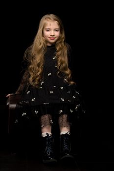 Cute little girl in a beautiful dress on a black background. Studio photo.