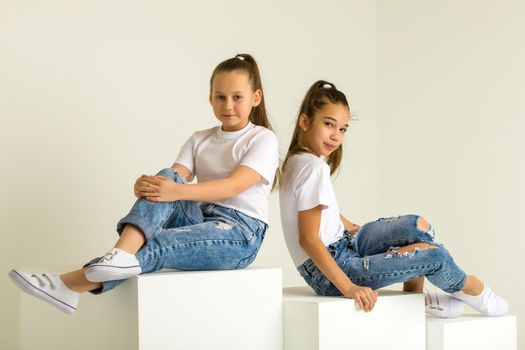 Two little girls posing in the studio on white cubes. The concept of tenderness and beauty.