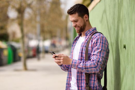 Smiling young man looking his smart phone in urban background. Guy wearing casual clothes. Lifestyle concept.