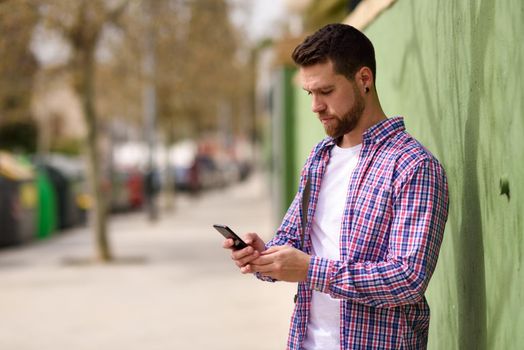 Young man looking his smart phone in urban background. Guy wearing casual clothes. Lifestyle concept.