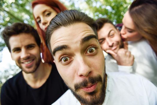 Group of friends taking selfie in urban background. Five young people wearing casual clothes.