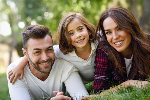 Happy young family in a urban park. Father, mother and little daughter laying on grass.