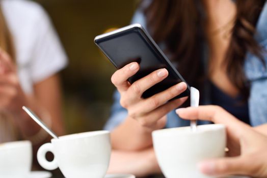 Close-up image of young girl hand with modern smartphone device, female hands typing text message via cellphone in a cafe bar.
