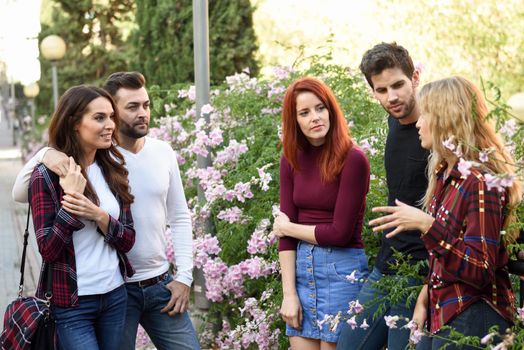 Group of young people together outdoors in urban background. Women and men sitting on stairs in the street wearing casual clothes.