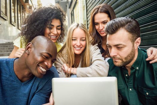 Multi-ethnic group of young people looking at a tablet computer outdoors in urban background. Group of men and woman sitting together on steps.