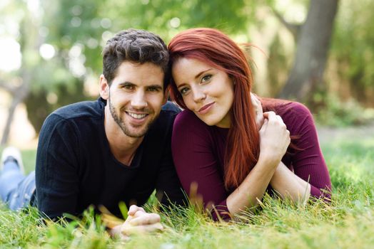 Beautiful young couple laying on grass in an urban park. Caucasian guy and girl wearing casual clothes. Redhead girl.